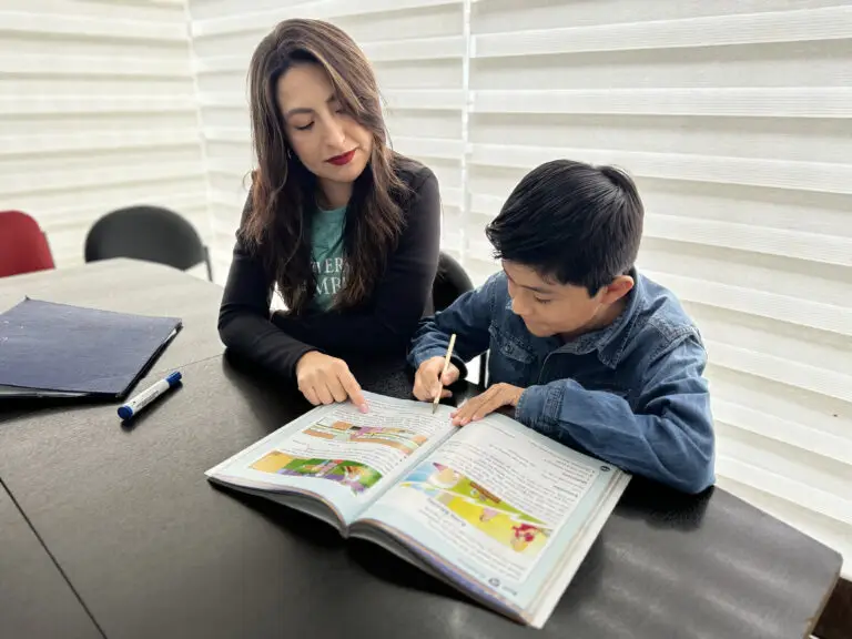 Profesora y niño alumno en clase revisando el libro de Cambridge.